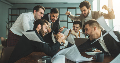 arm wrestling of two caucasian business people at work place, sitting at table in office, enjoy...