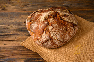 A fresh whole grain bread from the baker on a jute fabric on a rustic wooden background