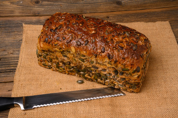 A fresh pumpkin seed bread from the baker on a jute fabric and a bread knife on a rustic wooden background.