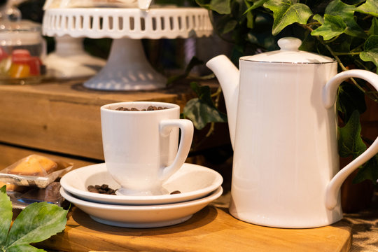 Close up image of porcelain teacup and teapot with fake plant decoration on a wooden table.