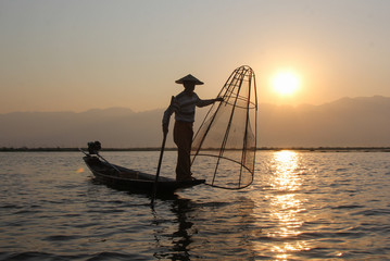 Myanmar fisherman of the Inle Lake at the dawn fishes well-known method with the  bamboo basket