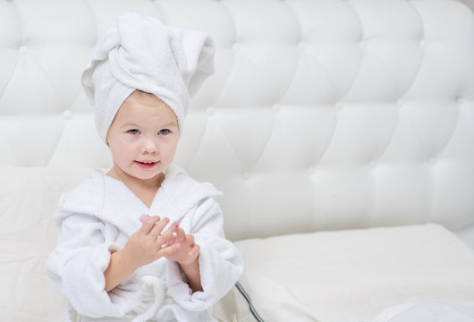 Little cute girl with a towel on her head does a manicure in her bedroom