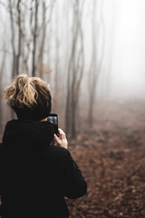junge Frau im Wald macht Fotos mit ihrem Mobiltelefon an einem trüben Herbsttag
