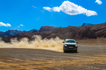 Obraz na płótnie Canvas SUV raises clouds of dust on a mountain plateau