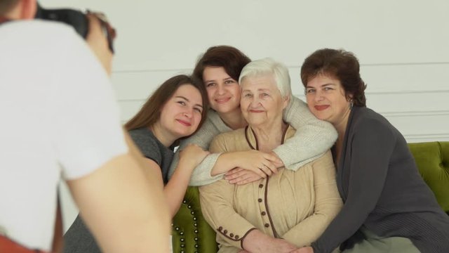 Photographer is taking pictures of an elderly white-haired woman with her granddaughters. The multi-generations family enjoys togetherness 
