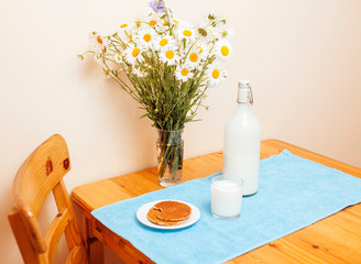 Simply stylish wooden kitchen with bottle of milk and glass on table, summer flowers camomile, healthy foog moring concept close up