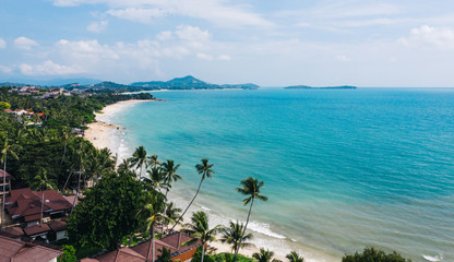 Aerial scenery view of white sand shore with turquoise clear sea water. Bird's eye panoramic view of picturesque lagoon with hotels on beach. Populated island in Thailand