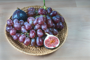 red grapes and fresh fig fruits in a straw basket on a light wooden background