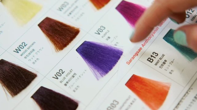 The client of hair salon chooses the color of hair dyeing on catalog. Close up.