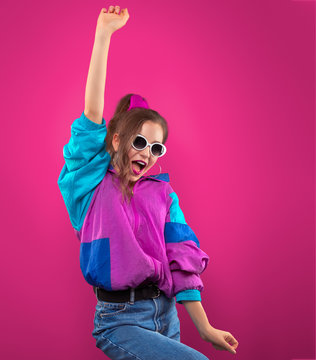 Fashion DJ girl in colorful trendy jacket enjoys dancing music 90s. Teenager Girl in vintage retro sunglasses dances at the disco party of 80s vibes. Fashionable young model on purple color.