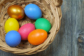 Colorful Easter eggs in the basket on the wooden surface