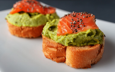 Salmon bruschettas with avocado on a black background, decorated with chia seeds.