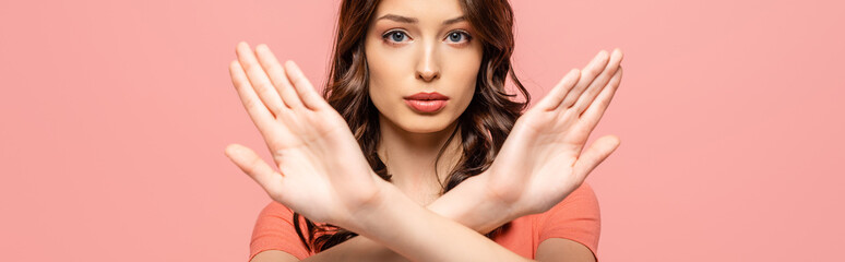 panoramic shot of serious young woman showing stop gesture while looking at camera isolated on pink