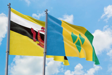 Saint Vincent And The Grenadines and Brunei flags waving in the wind against white cloudy blue sky together. Diplomacy concept, international relations.