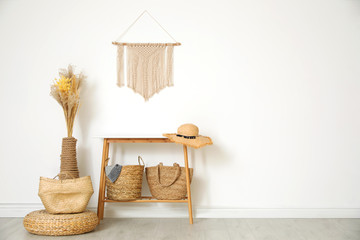 Stylish room with wooden table and wicker bags near white wall, space for text. Interior design