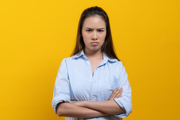 Angry woman standing crossed arms and stare at camera isolated on yellow background.