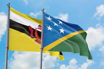 Solomon Islands and Brunei flags waving in the wind against white cloudy blue sky together. Diplomacy concept, international relations.
