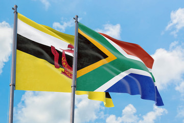 South Africa and Brunei flags waving in the wind against white cloudy blue sky together. Diplomacy concept, international relations.