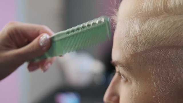 The hairdresser cuts dyed hair female client with scissors. A short pixie haircut and shaved temples . Ornament on the hair.