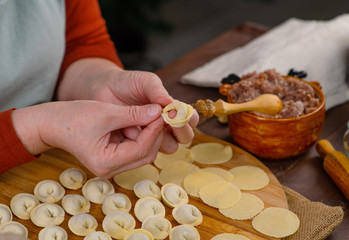 Obraz na płótnie Canvas Woman cook sculpts dumplings with his hands, close-up. On the table is minced meat and rolled circles of dough