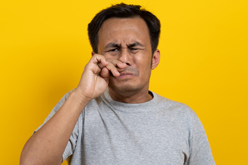 Face expression of human.  Asian male smelling disgusted odor and pinching his nose in studio shoot yellow background.