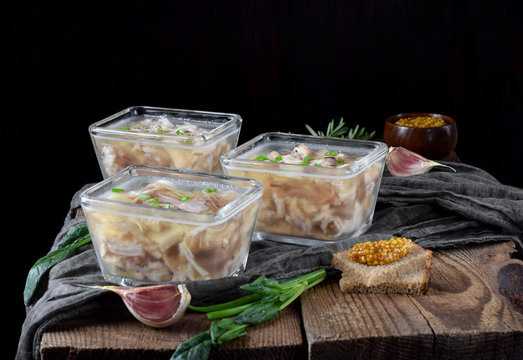 Holodets with chicken and pork meat in glass portion bowls against the dark background
