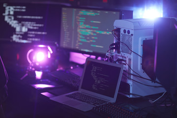 Background image of various computer equipment with programming code on screens in dark room, cyber...