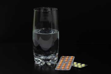 pills and glass of water on black background