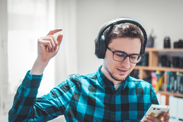 Enjoying music at home: Young Caucasian man is listening to music with headphones. Blue checked...