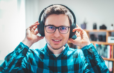 Enjoying music at home: Young Caucasian man is listening to music with headphones. Blue checked...