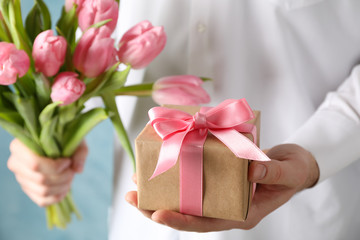 Man holds bouquet of pink tulips and gift on blue background, close up