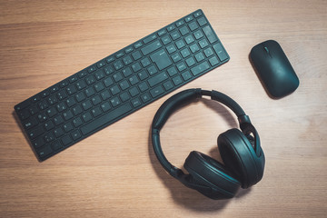 Workspace media concept: Black wireless headphones, keyboard and mouse on wooden desk