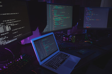 High angle view at various computer equipment with programming code on screens on table in dark...