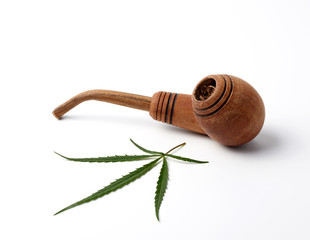 wooden smoking pipe and green hemp leaves on a white background