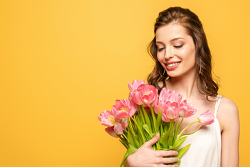 happy young woman holding bouquet of pink tulips isolated on yellow