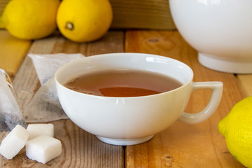 tazza di tè con teiera, zollette di zucchero, limone e bustine su fondo di legno