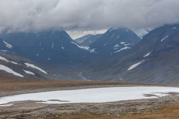 Fototapeta na wymiar Beautiful wild nature of Sarek national park in Sweden Lapland with snow capped mountain peaks, river and lake, birch and spruce tree forest. Early autumn colors in stormy weather. selective focus
