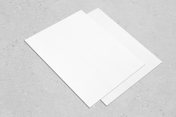 Closeup of two empty white rectangle vertical poster mockups lying diagonally on neutral grey...