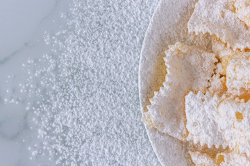 Frappe di carnevale, dessert italiano cucinato a febbraio, sul piatto bianco e fondo di marmo, spazio del testo