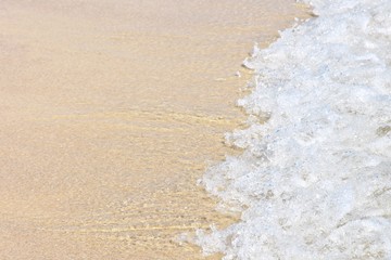 Transparent blue sea wave with white foam on a clean sandy shore, selective focus. turquoise ocean water with splashes. Summertime. Empty sand beach with beautiful  clean wave background. Summer rest