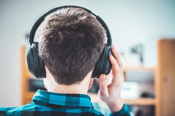 Enjoying music at home: Young Caucasian man is listening to music with headphones, back of the head