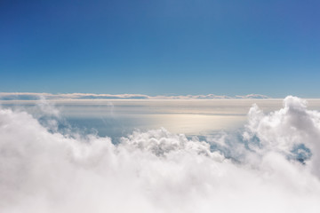 Beautiful aerial view at sunny peaceful surface of sea water and white fluffy clouds in clear blue sky as seen from 2000 metres highness. Amazing idyllic natural photo background.