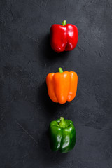 Green, orange and red bell peppers. Black background. Top view. Space for text.