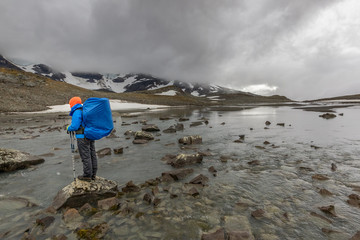 female hiker with backpack at Kungsleden trail admiring nature of Sarek in Sweden Lapland with mountains, rivers and lakes, birch and spruce tree forests. Early autumn colors in stormy weather