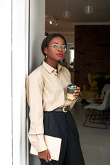 Young african woman is going away from cafe after her coffee break. She holds her tablet and looking at camera.