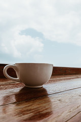 Close up Coffee cup on the wooden table with the cloudy sky for background design concept