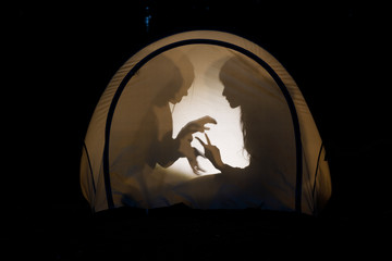 Children making shadow puppets in a camping tent at night