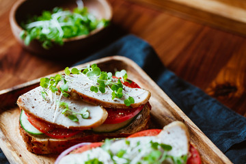 Sandwiches with turkey meat and fresh vegetables served with microgreens on a wooden plate