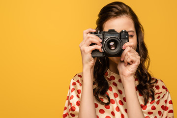 young woman taking phone on digital camera isolated on yellow