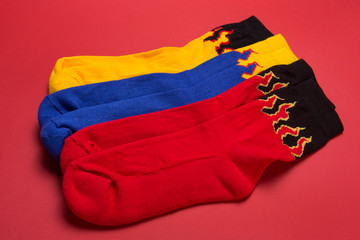 three pairs of socks, blue, red and yellow, with a flame pattern, lie on a red background